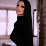 A long-haired brunette in a black bodysuit poses against a stone wall.