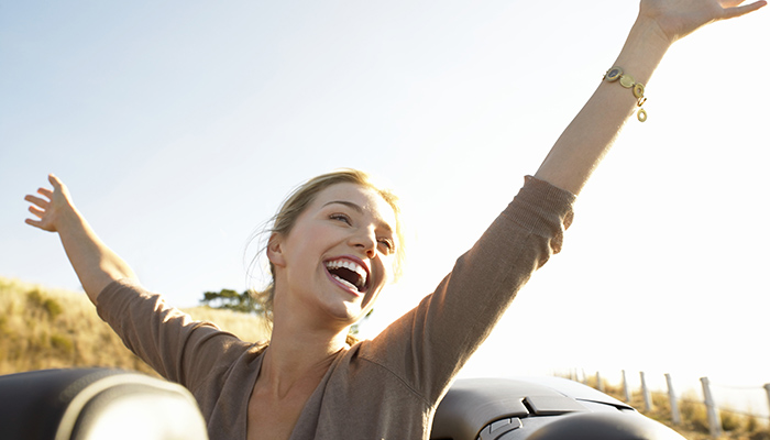 Young Woman Sits in the Back of a Convertible, Her Arms in the Air, Laughing With Joy