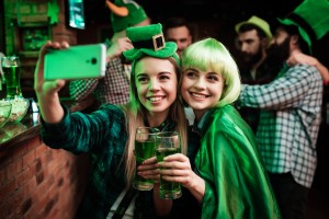 Two girls in a wig and hat make selfi at the bar. They celebrate St. Patrick's Day. They are having fun.