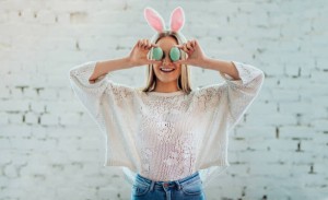 Portrait of young beautiful woman with bunny ears holding Easter egg on white wall background.