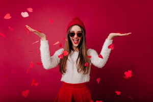 joyful-long-haired-girl-in-knitted-hat-having-fun-in-valentine-s-day-good-looking-brunette-lady-in-white-sweater-standing-under-heart-confetti