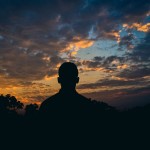 Silhouette of a man looking at a dramatic sunset sky with clouds.