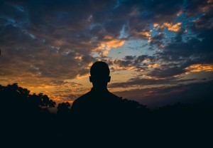 Silhouette of a man looking at a dramatic sunset sky with clouds.