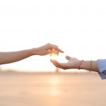Two hands reaching toward each other against a sunset sky.