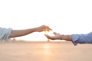 Two hands reaching toward each other against a sunset sky.