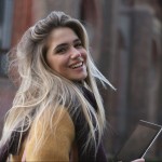 Smiling girl with tablet in hands, looking over shoulder, on the street.
