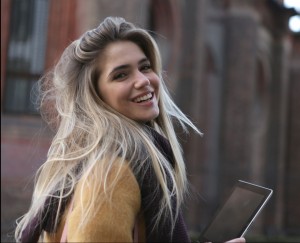 Smiling girl with tablet in hands, looking over shoulder, on the street.