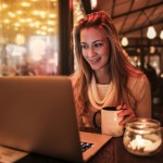 Step2Love woman in a cozy sweater using a laptop at a cafe with a cup of coffee.